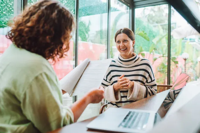 Two females sat at a table in front of a laptop