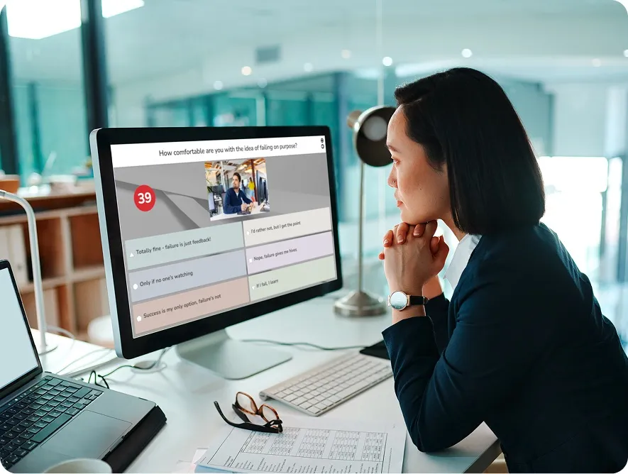A professional woman at a desk looking at a computer screen displaying a Kahoot! poll about comfort with failure.