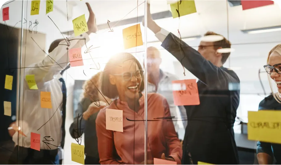 People sticking post-it notes to the walls of a glass wall meeting room