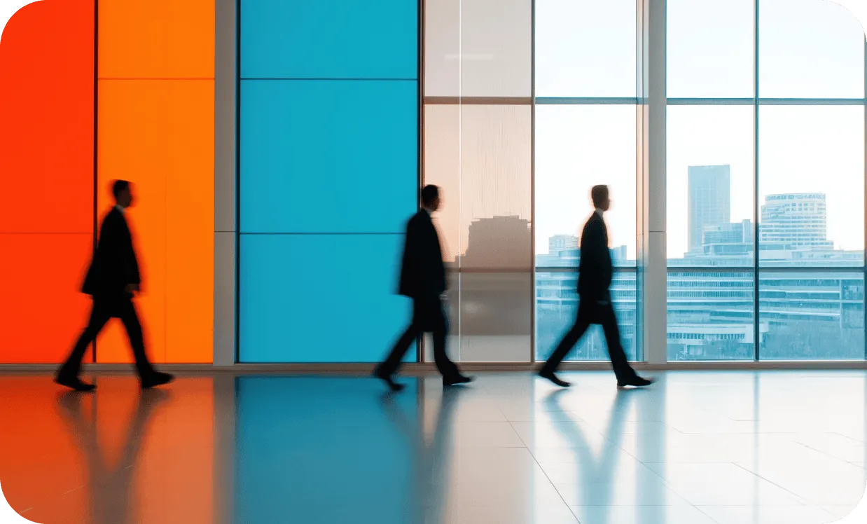 Three blurred silhouettes of business professionals walking through a modern office corridor with orange and blue walls