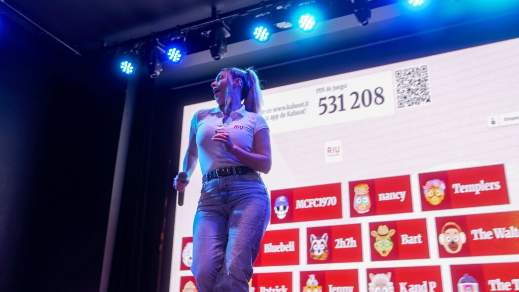 RIU Hotels & Resorts Entertainer A female RIU entertainer is on stage engaging an audience using Kahoot!