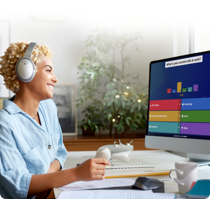 A woman with blonde curly hair wearing silver headphones smiles while looking at her computer. The monitor displays a live Kahoot! poll with colorful bar chart results.